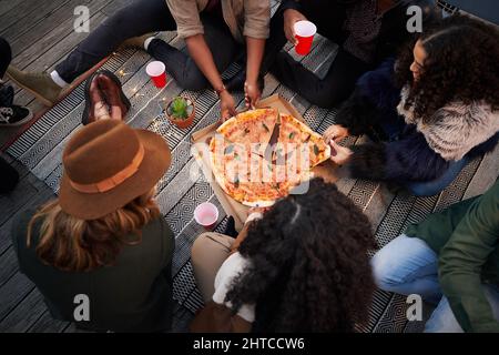 Un groupe d'amis divers qui s'occupe de pizzas à manger tout en étant assis sur la terrasse sur le toit de la ville Banque D'Images