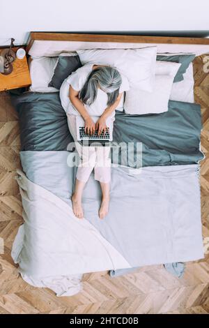 Image cinématographique d'une femme âgée à tête argentée utilisant un ordinateur portable et travaillant à domicile Banque D'Images