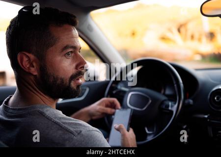 beau jeune homme utilisant son smartphone tout en attendant assis à l'intérieur de sa voiture, loisir et technologie de communication concept Banque D'Images