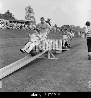 Laing Sports Ground, Rowley Lane, Elstree, Barnett, Londres, 20/06/1987. Deux hommes poussent chacun une femme dans une brouette tenant un seau d'eau au-dessus d'un pont en bois, l'un des obstacles de la compétition de style « c'est un Knockout » lors de la Journée de la famille 1987 au terrain de sport de Laing. Les attractions de la Journée de la famille de cette année-là incluent : tours en montgolfière, tours en hélicoptère, tours en château et parc d'expositions, stands, concours de style « It's a Knockout » et tournois de tennis et de football à six. Des membres de la troupe d'Eastenders ont fait une apparition et sont entrés dans une partie de la compétition de football Banque D'Images