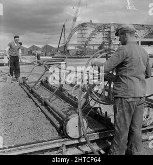 RAF Gaydon, Gaydon, Stratford-on-Avon, Warwickshire, 01/06/1954. Un ouvrier qui utilise un compacteur Holman pendant le béton d'une piste ou d'un tablier d'avion à l'aérodrome de Gaydon. Les travaux de construction d'une nouvelle piste à l'aérodrome de Gaydon ont commencé au début de 1952. Ce contrat a été suivi d'un deuxième contrat pour la construction de plus de 100 bâtiments Easiform, de 23 huttes de Nissen et de bâtiments du ministère de l'Air. En 1954, Laing a commencé à construire deux nouveaux hangars d'avion à l'aérodrome. Banque D'Images