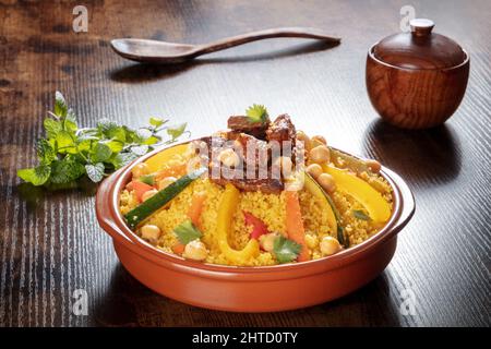 Viande et légumes couscous, cuisine marocaine traditionnelle, avec coriandre fraîche et menthe. Plat arabe festif sur une table en bois rustique sombre Banque D'Images