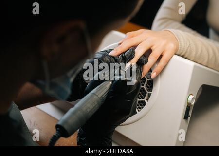 Vue rapprochée en grand angle d'une manucuriste féminine méconnue qui retire du gel vernis ou de l'acrylique des ongles à l'aide d'une machine de manucure. Banque D'Images