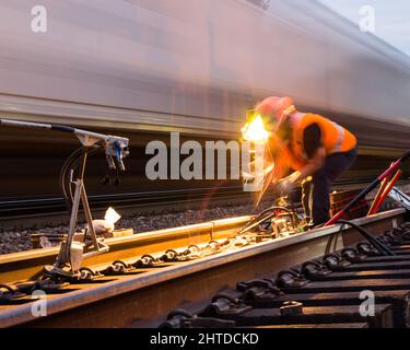 Travailleur dans le processus de réparation de soudure de voie de chemin de fer avec un train de marchandises passant Banque D'Images