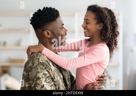 Vue latérale d'un père noir en uniforme militaire qui embrasse un enfant Banque D'Images