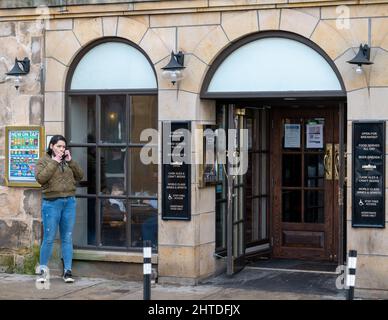 25 février 2022. High Street, Elgin, Moray, Écosse. C'est une femme qui est allée à l'extérieur du Pub pour avoir une fumée tout en bavardant sur son téléphone mobile Banque D'Images