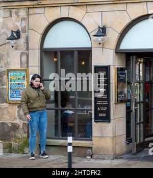 25 février 2022. High Street, Elgin, Moray, Écosse. C'est une femme qui est allée à l'extérieur du Pub pour avoir une fumée tout en bavardant sur son téléphone mobile Banque D'Images