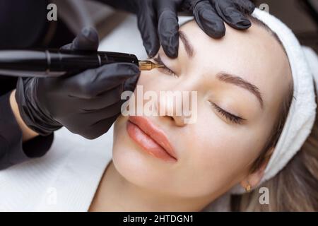 Gros plan d'une femme, dans un salon de beauté avec ses yeux fermés, un cosmétologue fait le maquillage permanent des paupières. Professionnel en gants noirs et avec un Banque D'Images