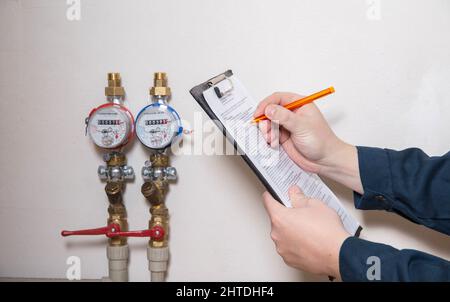 Un homme écrit les relevés des compteurs d'eau avec un stylo sur papier. Le concept de payer pour les services publics. Augmentation du prix par mètre cube d'eau, fermer Banque D'Images