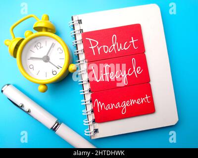 Horloge, stylo et bloc-notes écrits avec du texte gestion du cycle de vie des produits sur fond bleu. Banque D'Images