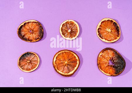 Six coupes différentes d'oranges séchées dans un arrangement régulier sur une surface violette. Banque D'Images