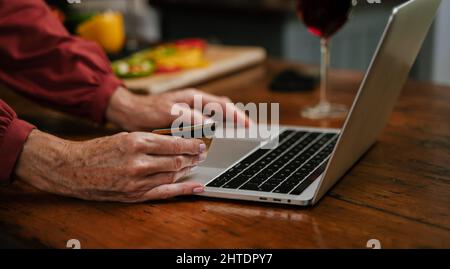 caucasien senior homme faisant le paiement en ligne tandis que la femme cuisine dîner Banque D'Images