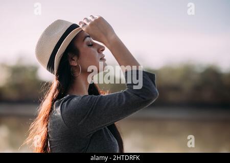 Gros plan de la femme latine brunette avec chapeau se détendant sur un quai au bord de la rivière. Concept de déconnexion dans la nature Banque D'Images