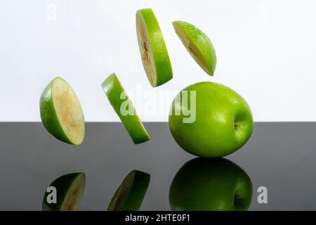 Gros plan d'anneaux de pomme coupés dans l'air près d'une pomme verte entière sur une surface noire Banque D'Images