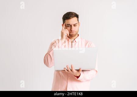Portrait d'un jeune homme sérieux debout avec un ordinateur portable pour lire des informations, regarder des vidéos, travailler à distance sur fond blanc isolé. Banque D'Images
