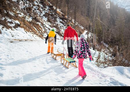 Père, fille et fils montant sur une pente de neige et tirant des traîneaux en bois, lors d'une belle journée ensoleillée d'hiver. Banque D'Images