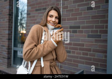 Femme élégante en manteau brun tient une tasse de café chaud à la main en automne à l'extérieur Banque D'Images