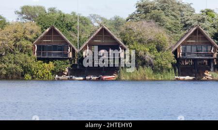 Trois chalets safari surélevés nichés dans les arbres et surplombant la rivière Chobe dans le parc national de Chobe, Botswana. Deux hommes travaillent sur un pont. Banque D'Images