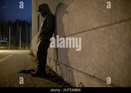Homme solitaire dans une veste sur une rue tout en s'appuyant sur le mur Banque D'Images