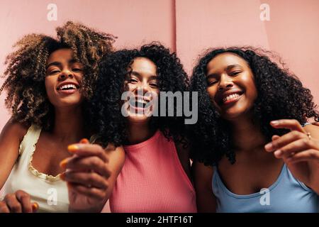 Trois amies joyeuses avec leurs cheveux bouclés riant ensemble et regardant l'appareil photo Banque D'Images