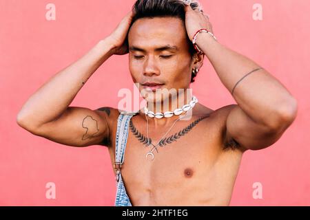 Gros plan d'un jeune homme avec des tatouages debout contre un mur rose avec des yeux fermés Banque D'Images