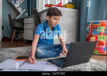 Enfant concentré assis sur son ordinateur portable pendant la leçon en ligne Banque D'Images