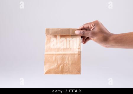 Image rognée d'une personne afro-américaine main tenant un sac à lunch en papier sur fond blanc Banque D'Images