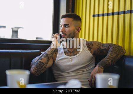 Jeune homme caucasien avec des tatouages frais assis dans le café parlant au téléphone Banque D'Images