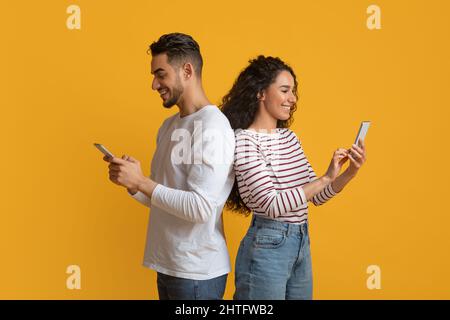 Dépendance de gadget. Jeune couple arabe tenant des smartphones et tenant debout dos à dos Banque D'Images