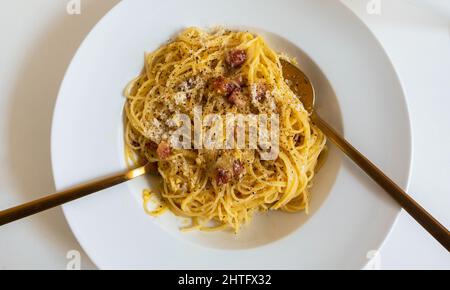 Spaghetti aux pâtes Carbonara dans un bol blanc avec une fourchette et une cuillère dorées Banque D'Images