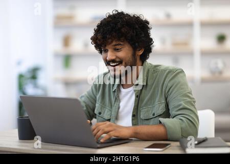 Joyeux jeune homme à la peau sombre utilisant un ordinateur portable moderne Banque D'Images