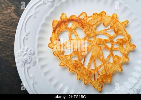 Crêpes ou crêpes en dentelle en forme de coeur sur plaque blanche sur fond rustique ancien.Table pour votre petit déjeuner préféré de la Saint-Valentin.Copie de la vue de dessus Banque D'Images