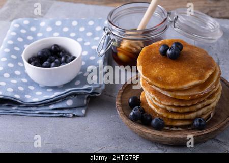 Vue en grand angle des crêpes empilées avec baies bleues et miel dans le pot sur la table Banque D'Images