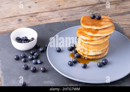 Vue en grand angle des crêpes empilées avec baies bleues et sirop dans l'assiette sur l'ardoise alimentaire Banque D'Images