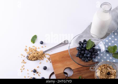 Vue en grand angle des baies bleues dans un bol et une bouteille de lait avec granola sur fond blanc Banque D'Images