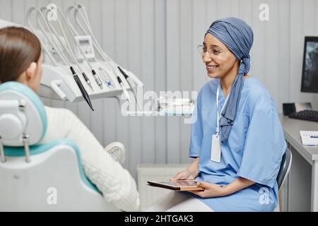 Portrait d'une jeune femme musulmane portant un uniforme médical tout en consultant un patient dans une clinique dentaire moderne Banque D'Images