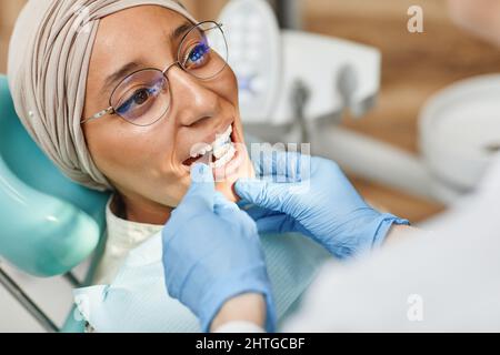 Gros plan de la jeune femme du Moyen-Orient en chaise dentaire, la bouche étant ouverte pendant l'examen en clinique Banque D'Images