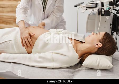 Portrait de la jeune femme enceinte se préparant à l'échographie en clinique médicale avec un médecin examinant le ventre Banque D'Images
