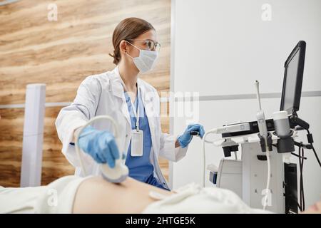 Portrait de la femme médecin à l'aide d'un échographe et portant un masque lors de l'examen d'une femme enceinte en clinique Banque D'Images