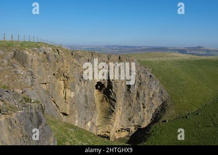 Carrière face près de Dirtlow Rake, près de Castleton, Derbyshire. Une immense face de roche rouge est clôturée d'en haut et montre les entrées de la grotte ci-dessous. Banque D'Images