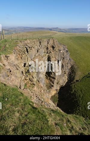 Carrière face près de Dirtlow Rake, près de Castleton, Derbyshire. Une immense face de roche rouge est clôturée d'en haut et montre les entrées de la grotte ci-dessous. Banque D'Images