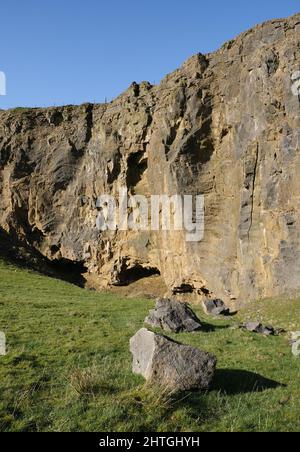 Carrière face près de Dirtlow Rake, près de Castleton, Derbyshire. Une immense face de roche rouge est clôturée d'en haut et montre les entrées de la grotte ci-dessous. Banque D'Images