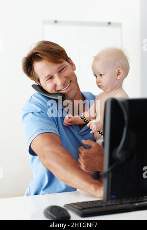 J'ai reçu un message important pour vous Papa. Photo d'un père à son bureau tenant un petit enfant tout en parlant au téléphone. Banque D'Images