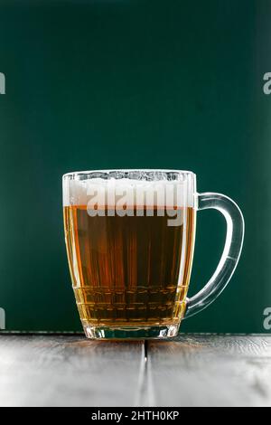 Mug avec bière traditionnelle irlandaise pâle sur fond vert foncé. Bulles dans un verre de bière. Banque D'Images