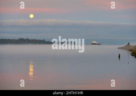 Ensemble pleine lune le matin. S'amarrer sur le fleuve Fraser alors qu'un cargo voyage en amont. Richmond, Colombie-Britannique, Canada. Banque D'Images