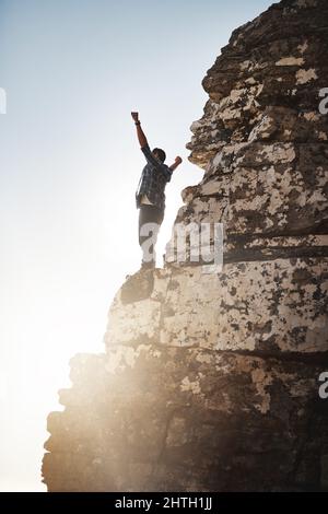 Je roi du monde. Plan d'un jeune homme debout sur une falaise de montagne avec ses bras levés. Banque D'Images