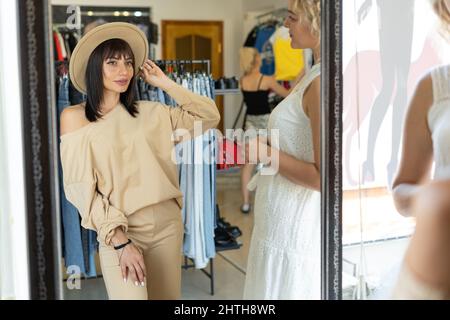 Femme essayant un chapeau dans un magasin de centre commercial. Un client effectue un achat dans une boutique. Le vendeur aide le client. Femme élégante devant un miroir dans un Banque D'Images