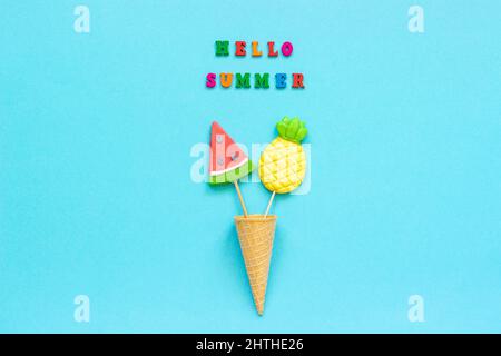 Bonjour été texte coloré, ananas et pastèques dans le cône de gaufre de glace sur fond de papier bleu. Concept vacances ou vacances Créativ Banque D'Images
