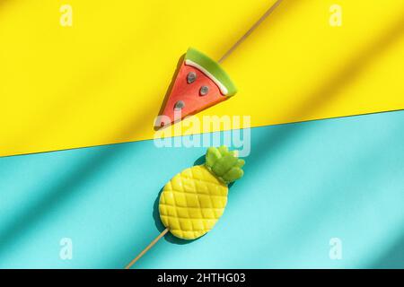 Fruits d'été ananas et pastèques sucettes sur bâton sur fond bleu jaune avec lumière et ombre dures. Concept Creative vue de dessus modèle GRE Banque D'Images