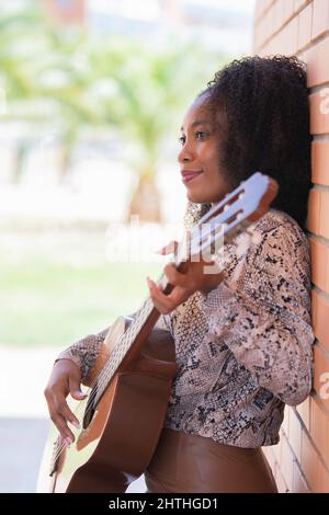 Jeune femme penchée sur un mur de briques jouant de la guitare regardant loin Banque D'Images